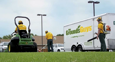 Three Grounds Guys employees performing lawn cleanup work next to company trailer.